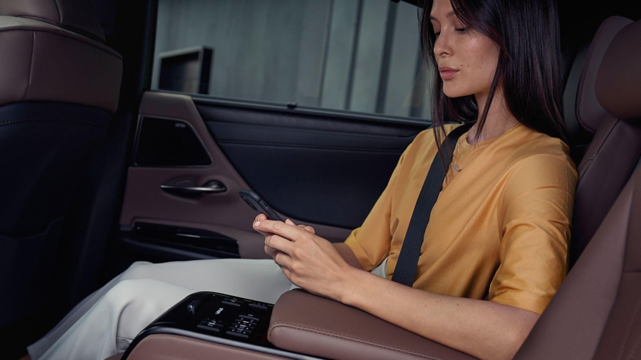 אשה יושבת במושב אחורי במכונית של לקסוס ומשתמשת בטלפון נייד.
