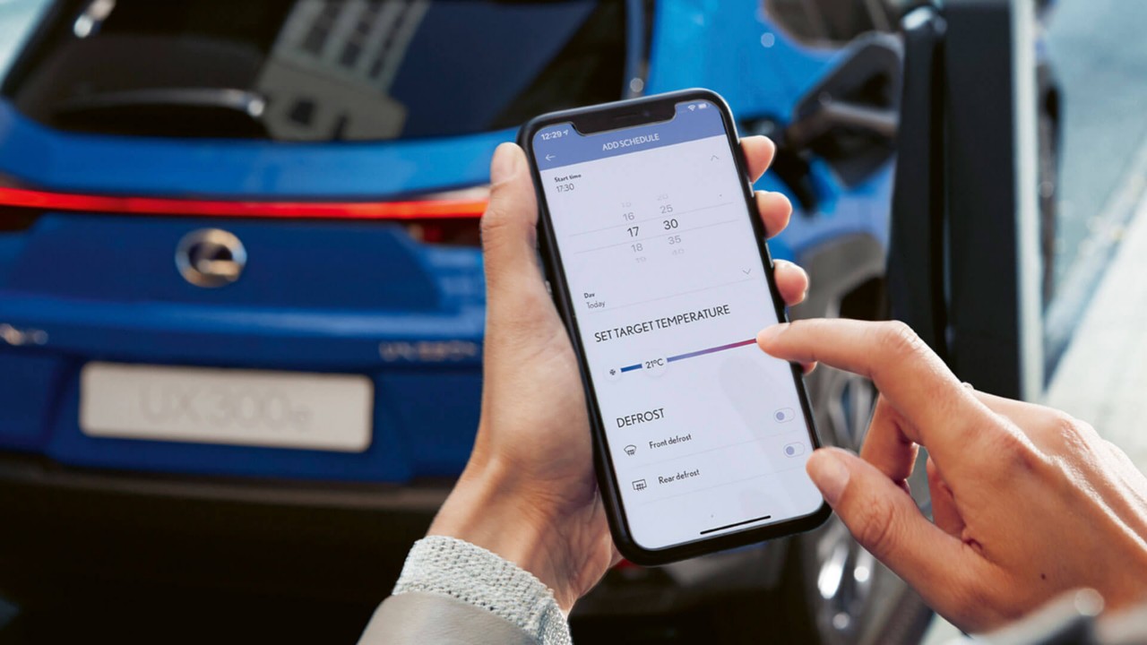 אדם משתמש בטלפון נייד עם אפליקציית LEXUS LINK ברקע מכונית לקסוס UX
